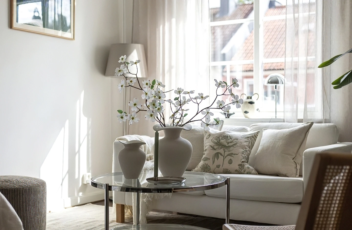 Ljust vardagsrum med vit soffa, glassbord och blomstervaser.
